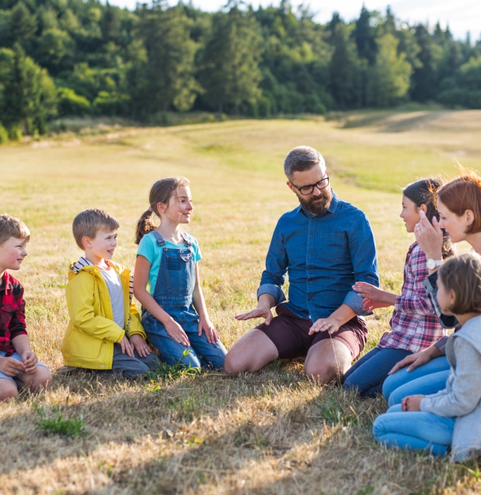 Group of school children with teacher on field trip in nature, talking. Group of school children with teacher on field trip in nature, sitting and talking.